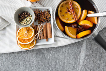 christmas and seasonal drinks concept - pot with hot mulled wine, orange slices, aromatic spices and ladle on grey background
