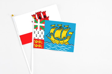 Saint Pierre And Miquelon and Gibraltar stick flags on white background. High quality fabric, miniature national flag. Peaceful global concept.White floor for copy space.