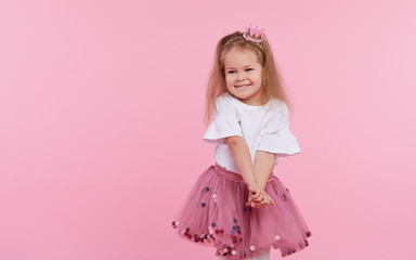 A cheerful little girl with in a tulle skirt and princess crown on her head isolated on a pink background. Celebrating a vibrant carnival for kids, birthday party, having fun  © oes