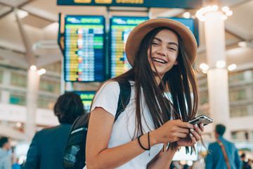 tourist with a backpack in a hat with a phone in his hands at the airport laughs joyfully - 302703469