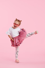 Happy childhood. Funny child girl in tulle skirt jumping and having fun isolated on pink...