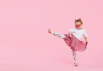 Happy childhood. Funny child girl in tulle skirt jumping and having fun isolated on pink...
