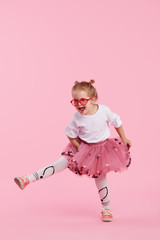Happy childhood. Funny child girl in tulle skirt jumping and having fun isolated on pink...