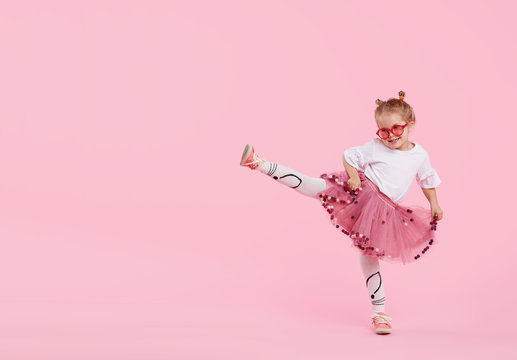 Happy childhood. Funny child girl in tulle skirt jumping and having fun isolated on pink background. Celebrating a vibrant carnival for kids, birthday party. True emotions. Space for text