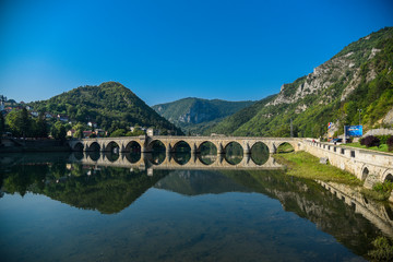 Fototapeta premium The Ottoman Mehmed Pasa Sokolovic Bridge in Visegrad, Bosnian mountains, with fantastic sky scape and river reflection. Bosnia and Herzegovina.