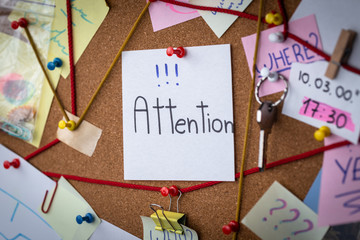 Attention concept. Close-up view of a detective board with evidence. In the center is a white sheet attached with a red pin with the text Attention