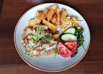 Piece of pork with fried potatoes and mushroom sauce. Fresh vegetable salad on a white plate
