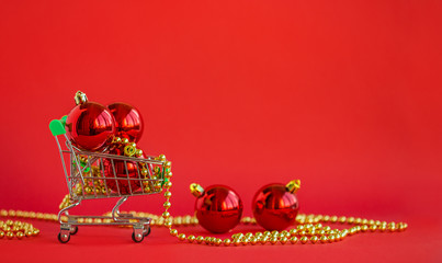 Gift Christmas balls in a miniature trolley and decorations on a red background. Christmas and New Year Sale.