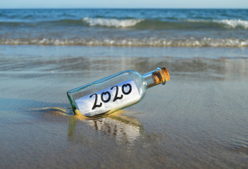 Obraz premium Happy New Year 2020, message in a bottle on the beach