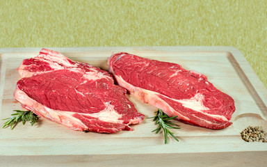 deux entrecôtes de boeuf crues sur planche à découper