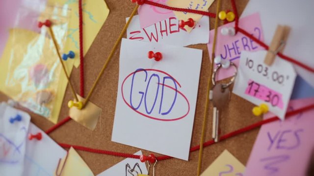 God search concept. Close-up view of a detective board with evidence. In the center Girl's hand pins a white sheet of paper with the inscription God