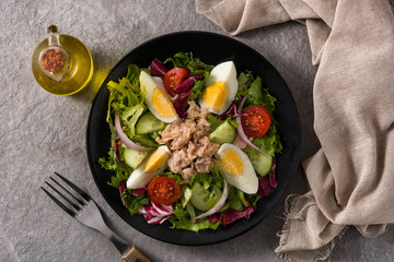 Salad with tuna, egg and vegetables on black plate and gray background. Top view	