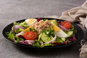 Salad with tuna, egg and vegetables on black plate and gray background	