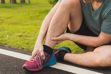 Naklejka premium Ankle sprained. Young man suffering from an ankle injury while running at park. Healthcare and sport concept.
