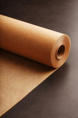 A roll of unfolded brown parchment paper, for baking food in on a dark background, top view.