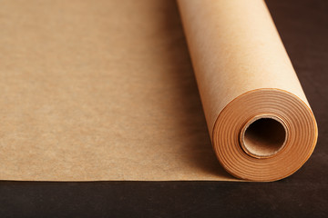 A roll of unfolded brown parchment paper, for baking food in on a dark background, top view.
