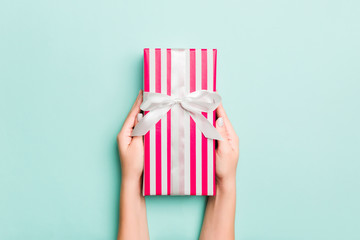 Woman hands give wrapped christmas or other holiday handmade present in colored paper. Present box, decoration of gift on Blue table, top view with copy space