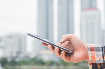 close up handsome businessman using hand typing smartphones and touch screen working search with app devices outdoor in city with sunrise and building background. 5G technology connecting the world.