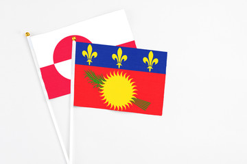 Guadeloupe and Greenland stick flags on white background. High quality fabric, miniature national flag. Peaceful global concept.White floor for copy space.