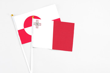Malta and Greenland stick flags on white background. High quality fabric, miniature national flag. Peaceful global concept.White floor for copy space.