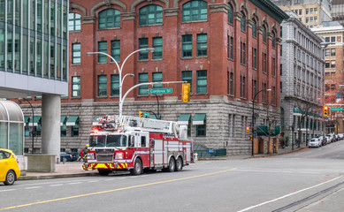 Fire truck responding to an alarm in the city. The fire truck is parked at an intersection in downtown surrounded by buildings. A fire fighter is getting in the vehicle.  W Cordova Street, Vancouver