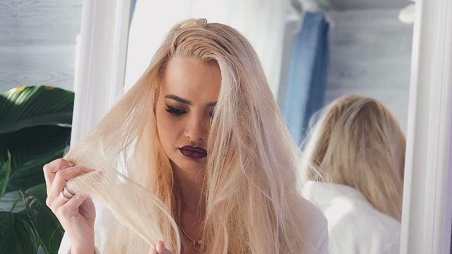 The girl is entangled in her hair. Blonde sad looks into the camera and touches naughty hair