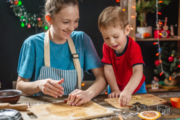 Mom and child son shape the dough for baking homemade holiday gingerbread. Family cooking in Christmas decorations