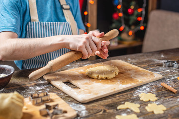 Woman rolls out the dough with a rolling pin and shapes festive gingerbread. Christmas time cooking delicious cookies.