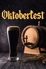 glass of beer near small keg with tap and wheat spikes on wooden table with Oktoberfest lettering