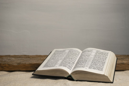 Open Holy Bible on a old wooden table and white wall background. Religion concept.