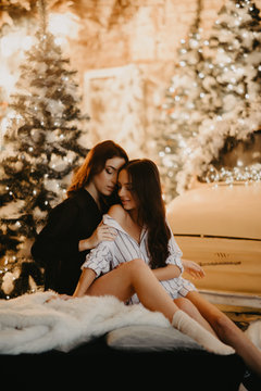 Lesbian Couple Sits Against Background Of Christmas Decorations And Retro Car.