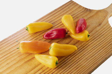 Trio of mini peppers multicolored, on wooden cutting board, on white background