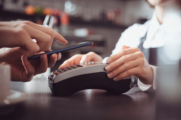 The client pays in the cafe with a mobile phone using NFC technology. Contactless payment by smartphone on a POS terminal.