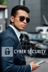 handsome and confident african american businessman in suit and sunglasses using smartphone with internet security illustration