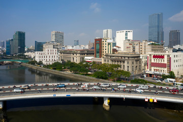 Fototapeta premium Wide Drone shot of Morning traffic on Khanh Hoi Bridge over Ben Nghe Canal separating districts four and one in Ho Chi Minh City. Background features financial and banking district