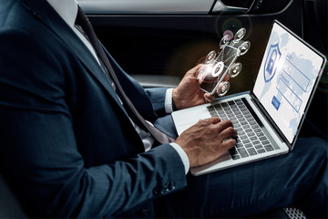 cropped view of african american businessman using laptop and smartphone in car with internet...