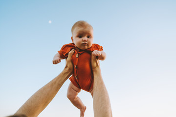 Infant baby being held up in the sky by father hands outdoor adorable child happy family lifestyle...
