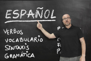 Male Spanish teacher pointing to some language concepts writen on a blackboard in the classroom....