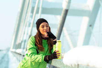 Young woman rest on the bridge and dring water afther jogging on snow