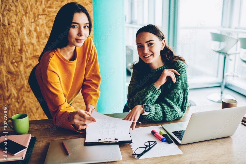 Poster portrait of successful female designers smiling at camera while working together on creating plan fo