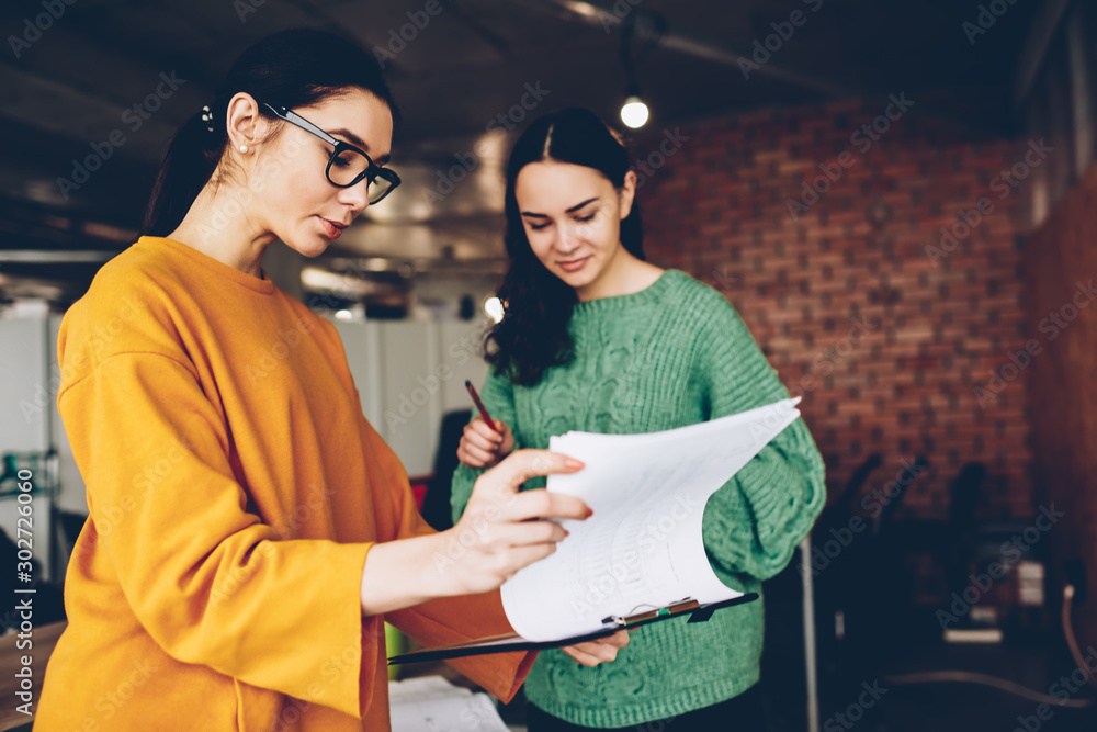 Poster two smart female architects checking building planning standing in office interior.clever women work