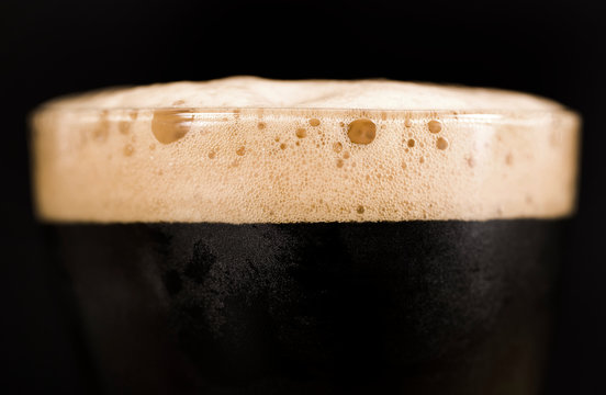 Glass of dark beer isolated on black background. Foam close up.