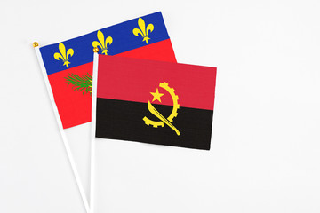 Angola and Guadeloupe stick flags on white background. High quality fabric, miniature national flag. Peaceful global concept.White floor for copy space.
