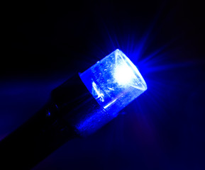 Single bright blue glowing led light with lens flare isolated on black background