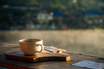 A cup of hot coffee with smoke on the wooden front of the lake view with sunlight at Ban Rak Thai,Mae Hong Son,Thailand.