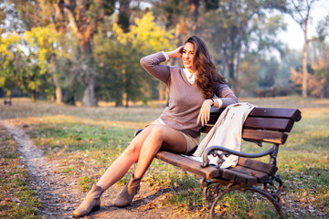 Beautiful young woman sitting on bench in park and smile