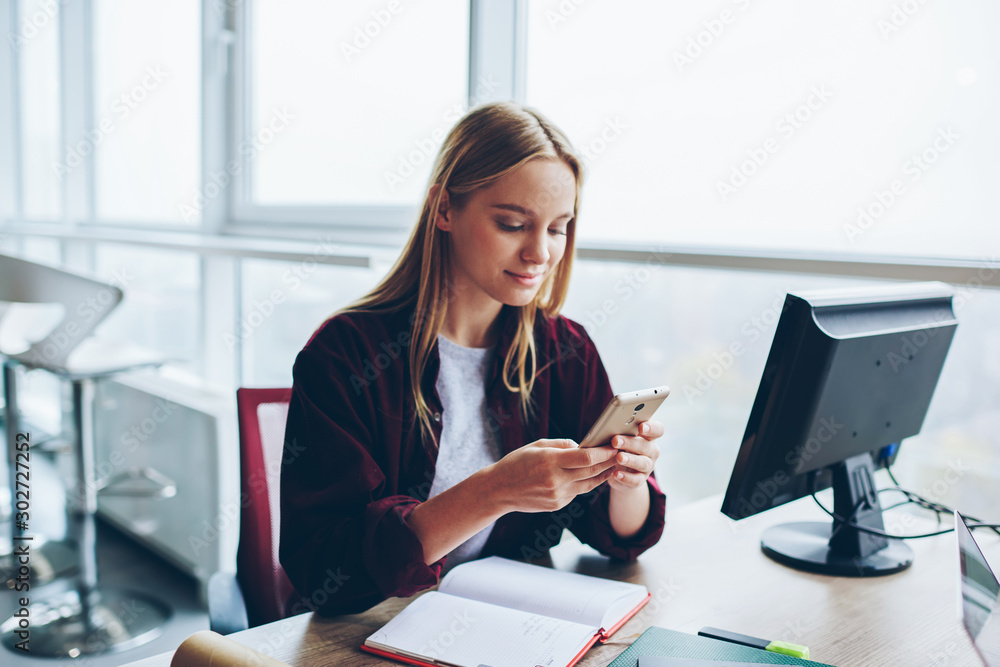 Poster positive blonde female blogger sending text message in social networks using smartphone, caucasian w