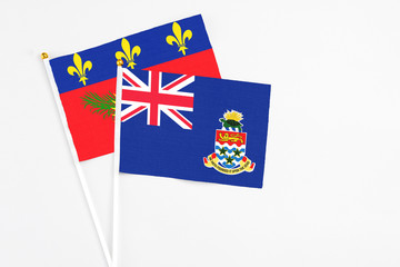 Fototapeta premium Cayman Islands and Guadeloupe stick flags on white background. High quality fabric, miniature national flag. Peaceful global concept.White floor for copy space.