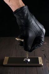 The hand of an attacker in a black glove opens the lock on a smartphone with a key. The concept of...