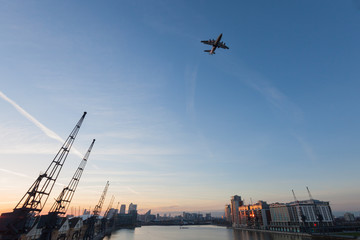 Passenger plane flying over the Thames River at sunset, Royal Victoria Dock, London, England
